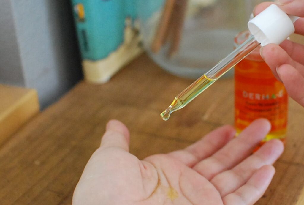 DERMA・E アンチリンクルトリートメントオイルの小瓶と手に落ちるオイルの画像