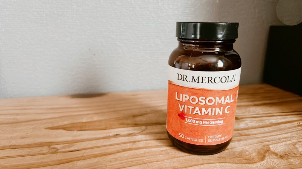 iHerbで購入したドクターメルコラのリポソームビタミンCのボトルが、木製の棚のすみで光を浴びている様子。