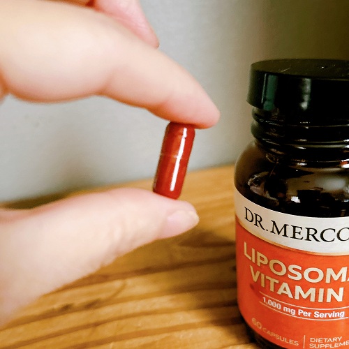 ドクターメルコラのリポソームビタミンCのカプセルを指でつまんでいる拡大写真。日本のサプリと比較してやや大きめのサイズ感が分かる。