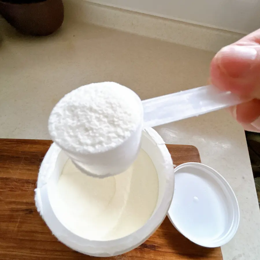 California Gold NutritionのCollagenUPボトルの口から、付属の計量スプーンで真っ白な無香料コラーゲン粉末をすくい上げた様子。粉末の質感とスプーンのサイズ感。