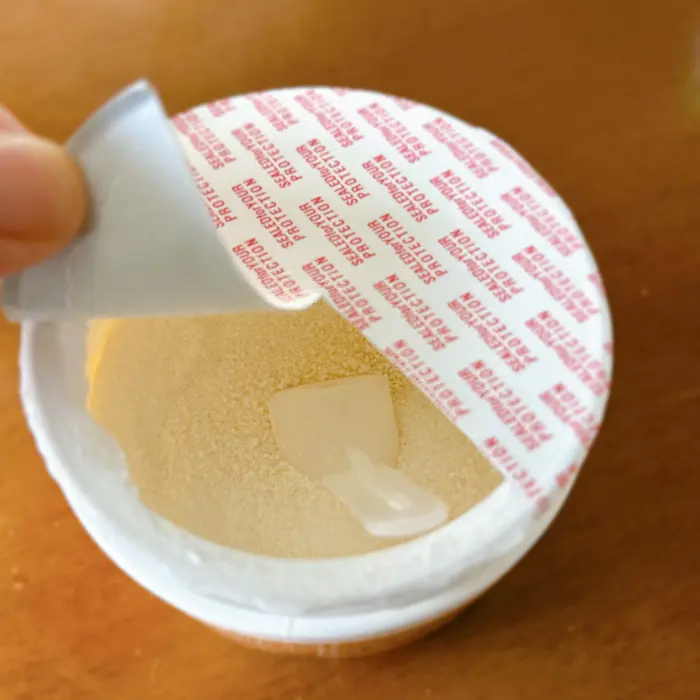 iHerbの粉末サプリメント(HydrationUP)の内蓋(シーリング)を全部剥がさず、半分だけ残して粉の飛び散りを防ぐ開封の工夫。付属スプーンが粉に刺さっている。