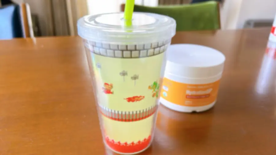 マリオのイラストが描かれた子供用ストロー付きタンブラーに入ったシトラスフレーバーの電解質ドリンクと、後ろに置かれたCalifornia Gold Nutrition HydrationUPのボトル。